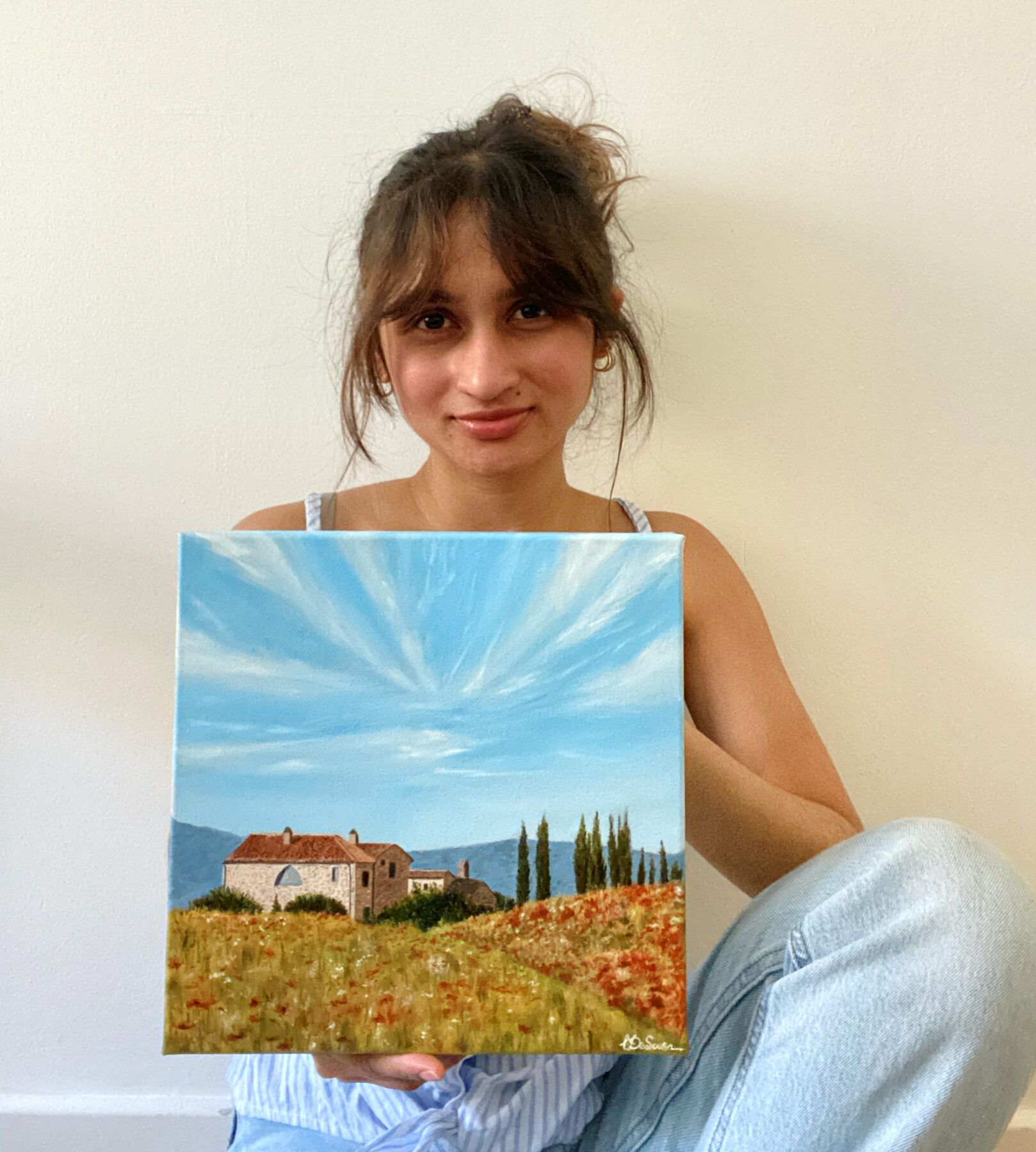 Liana De Sousa holding one of her paintings against a white wall — professional portrait